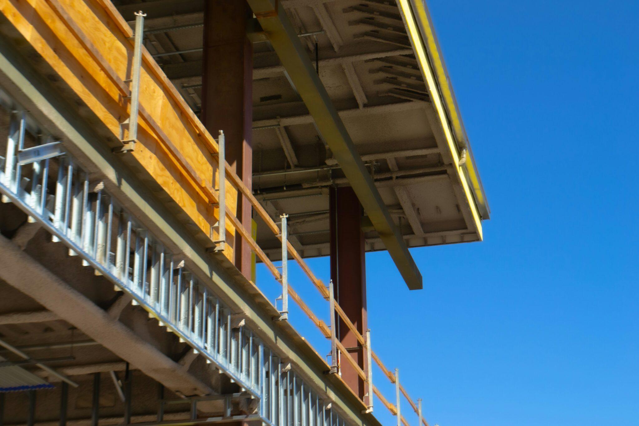 Gebäude in der Bauphase, mit Stahlträgern, offener Dachkonstruktion, daneben blauer Himmel
