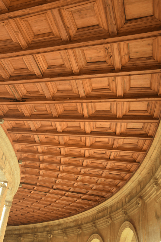Geschwungene Kassettendecke aus rötlichem Holz, darunter eine tragende Konstruktion aus Rundbögen
